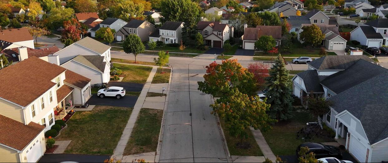 Aerial view of a suburban neighborhood with houses and trees displaying autumn colors.